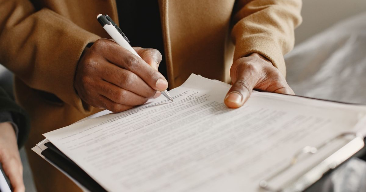 A person writing on a document attached to a clipboard.