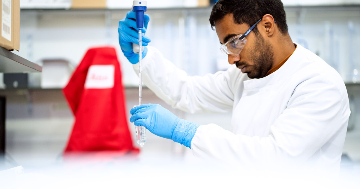 A scientist holds a pipette over a tube in a laboratory.