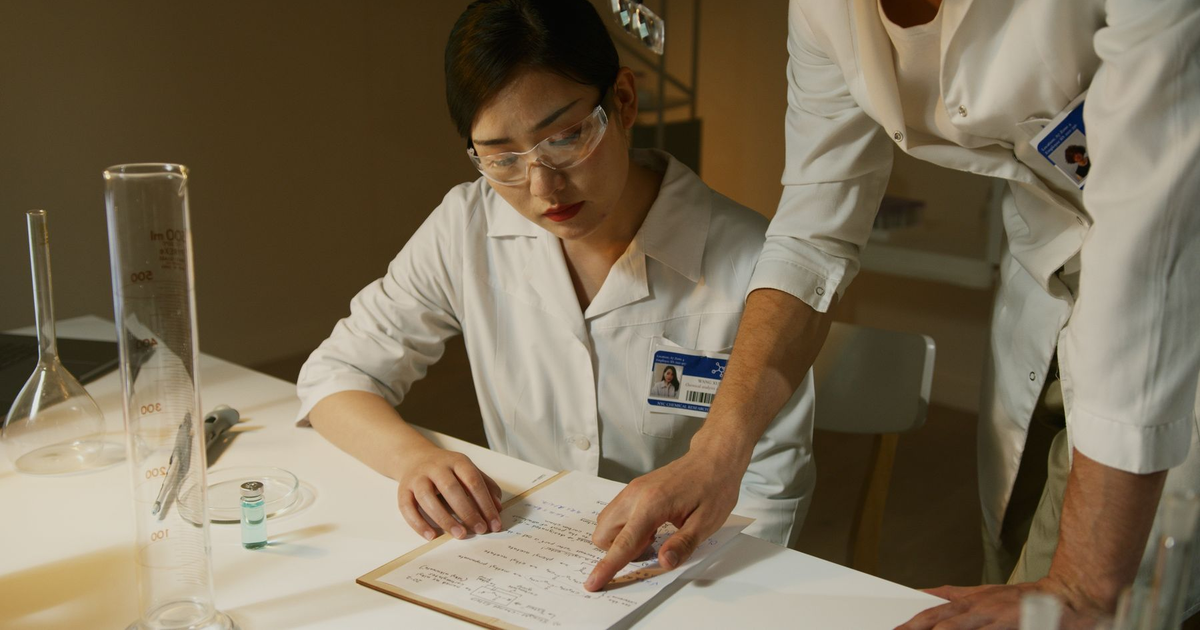 Two researchers read notes together at a laboratory table.