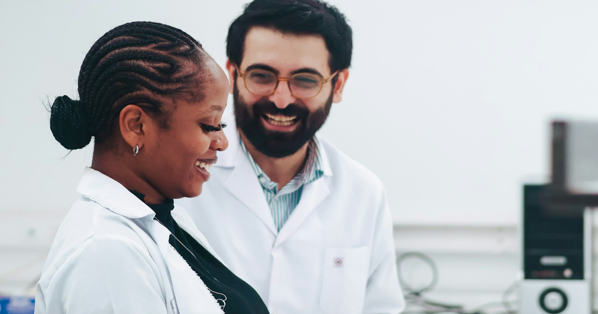 Photo: Amari Shutters / Unsplash (Unsplash License) Two scientists in white laboratory coats standing beside laboratory equipment.