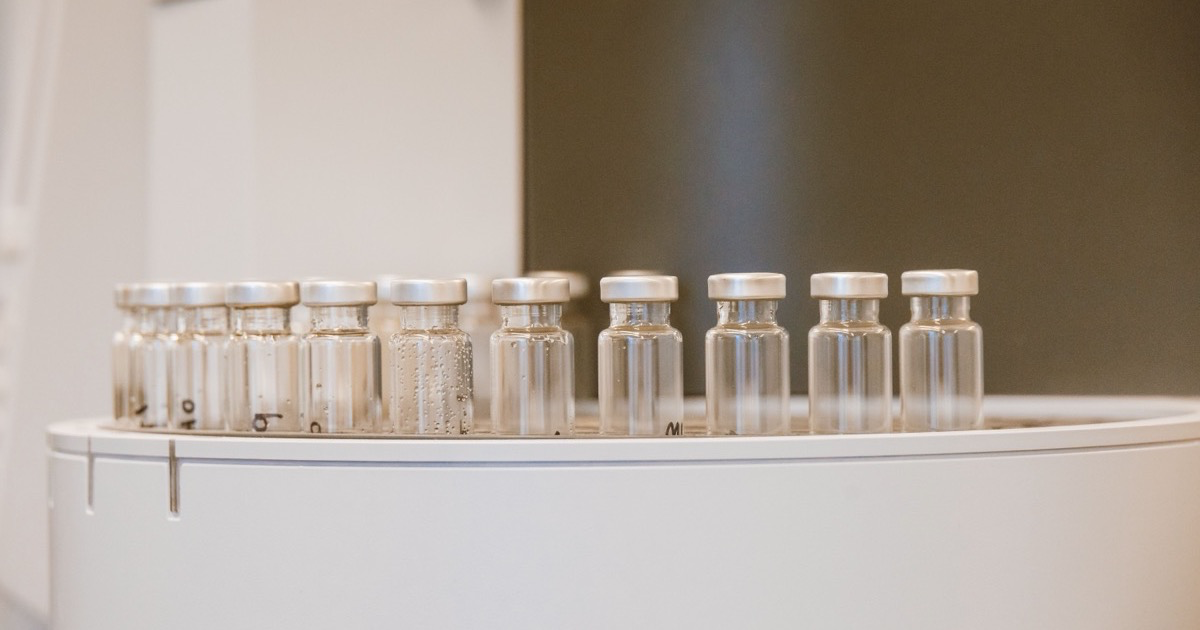 A row of small clear glass vials with silver crimp caps on top of a round white laboratory instrument