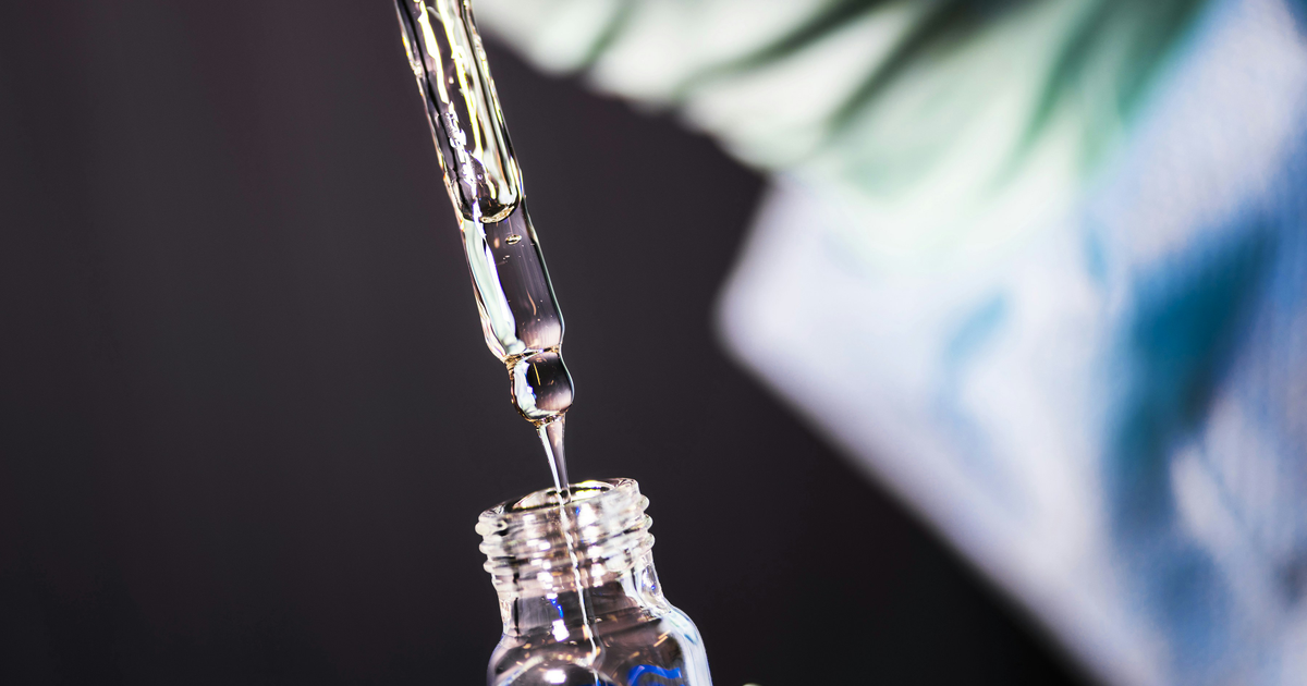 Photo: CDC / Unsplash (Unsplash License) A glass pipette drips clear liquid into a small glass vial against a dark background